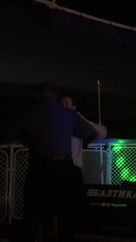 Two people are dancing on a boat at night. One person is wearing a dark shirt and pants, while the other is wearing a light-colored shirt and dark pants. They are holding each other and moving to the music. The boat has railings and a canopy overhead. There are lights in the background. The word "БАЛТИКА" is visible on a sign.