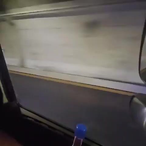 A red Porsche 911 is traveling through a tunnel at night. The camera is inside another vehicle, facing forward. The tunnel walls are concrete and lit by artificial lights. The road has yellow lane markings. The Porsche is visible in the camera's field of view, ahead of the camera. The camera has a phone mounted to it, displaying a map.