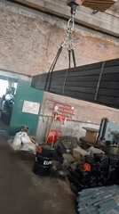 Crane lifts stack of black metal tubes in industrial facility
