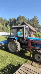 Man operates blue tractor with attachments in grassy field