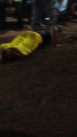 The video shows a person in a yellow gown crawling on their hands and knees on a patch of grass or dirt. They are surrounded by seated people, who seem to be watching. The lighting is dim, suggesting that the video was taken at night. The scene appears to be part of an event or performance.