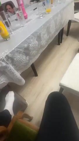 The video shows a room where four men are sitting on a couch. There is a table in front of them covered with a patterned tablecloth. On the table, there are several glasses, bottles of soda, and other containers. One of the men on the couch leans back. The camera pans across the room, showing furniture, including a shelf unit. There's an object that appears to be a pink sex toy on the table.