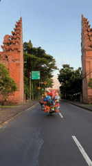 Balloon-laden motorbike spotted on Balinese road near traditional gates