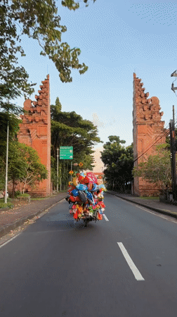 Balloon-laden motorbike spotted on Balinese road near traditional gates