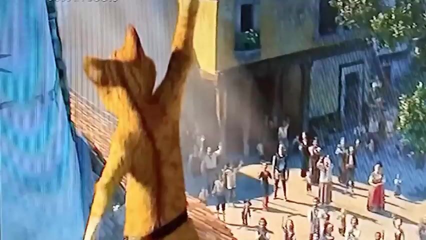 The video begins with a close-up of Puss in Boots, an anthropomorphic orange cat wearing a black hat and boots. He is in motion, raising his hat as if in a bow or greeting. The background is a blurred, light blue. The scene then shifts to a wider shot of Puss in Boots, who is standing still, looking directly at the camera with his sword sheathed at his side. The background remains a light blue. Subsequently, the video shows a street scene in a town with terracotta-tiled roofs and buildings. Two people, out of focus in the foreground, are raising their hands towards the sky. In the distance, Puss in Boots is seen jumping or flying through the air above the buildings.