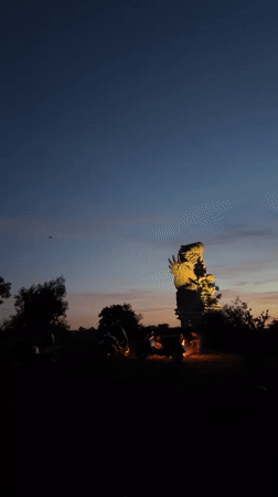 Illuminated bird sculpture draws motorcycle visitors at Indonesian dusk