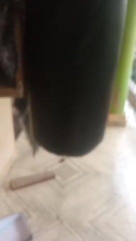 A video shows a person's foot kicking a punching bag. The punching bag is large and black. There is a xylophone on the floor to the left of the punching bag. The floor is tiled. There is a balcony with a railing in the background. It appears to be raining outside.