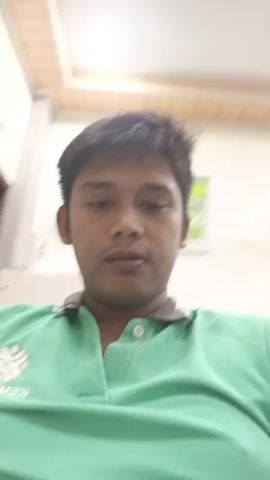 The video shows a close-up of a young man with dark hair and a green polo shirt. He is in what appears to be an indoor setting with a white ceiling and a framed picture on the wall behind him. The man is seen touching his hair and adjusting it with his hands. His facial expressions are neutral to slightly serious. The lighting suggests it is daytime.