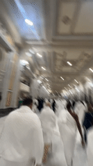Crowds in white fill an ornate hallway during a religious gathering.