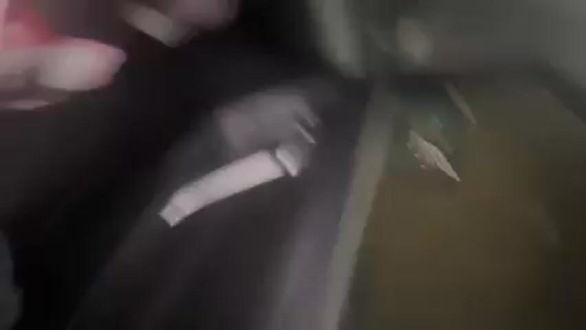 The camera is shaky and inside a car, facing forward. The driver's seat is visible, occupied by a person wearing black pants and white sneakers. In front of the seat are several items: an open can of Red Bull, a bag of cheese slices, and a package of candy. The car appears to be moving through a tunnel, visible through the windshield, with lights on the tunnel walls.
