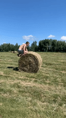 Balancing on a round hay bale in an open field