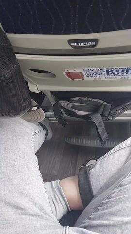 The video captures the interior of a moving vehicle, likely a double-decker bus or train, from a passenger's perspective.

At the beginning, the camera shows a person's legs, clad in light grey jeans and grey slippers, resting on a footrest. A black backpack with straps hangs from the seat ahead. The word "NEOPLAN" is visible on the seat structure. The camera then pans upwards, revealing the vehicle's interior, characterized by blue seats with a subtle wave pattern and light-colored handles. Blue LED strip lighting runs along the ceiling.

Further panning shows the upper deck of the vehicle, with the back of a person's head (with brown hair) visible in the foreground. The final shots look out through the front window of the upper deck, showing a blurred green landscape indicating the vehicle is in motion. Part of a blue curtain and the back of a seat are visible in the foreground. The weather outside appears bright but overcast. The setting suggests travel through a rural or suburban area, consistent with the given location context of Staro Slano, Bosnia and Herzegovina.