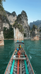 Longtail boat navigates emerald waters through Thailand's limestone cliffs