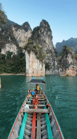 Longtail boat navigates emerald waters through Thailand's limestone cliffs