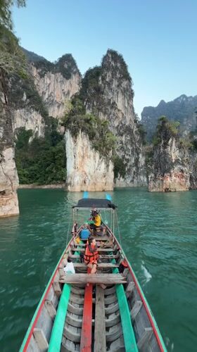 Longtail boat navigates emerald waters through Thailand's limestone cliffs