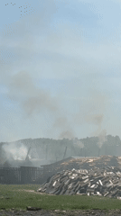 Rural fire burns near lumber mill in grassy field
