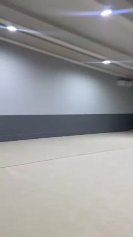 This media file captures a moment in what appears to be an indoor gym or fitness facility. The setting is characterized by its clean, modern design, with light-colored walls and flooring. In the background, there are several pieces of gym equipment, including what looks like a set of Swedish ladders, and a blue storage bin with various colorful items, possibly hula hoops, inside. The lighting suggests it is daytime, but the interior setting makes it difficult to determine external weather conditions.

The focal point of the video is a small, red squirrel perched on top of one of the Swedish ladder bars. The squirrel is the sole subject of the close-up shots, displaying its bushy tail and curious demeanor. It appears to be resting or observing its surroundings. The presence of the squirrel in an indoor, human-dominated space is a notable and unusual detail, suggesting a possible entry point or a surprising visitor. No people are visible in the media. The activity taking place is essentially the squirrel's presence and stillness within the gym. The emotions conveyed are primarily one of curiosity and slight surprise due to the unexpected animal in this environment. There is no visible text in the media. The location context provided, Novoye Lapino, Russia, places this scene in a specific geographical area.