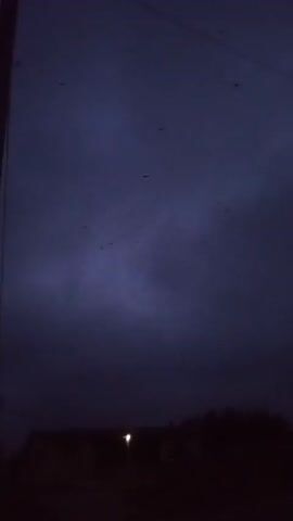 The video shows a dark, cloudy sky at night. The clouds are a deep blue and gray color. There are also power lines visible in the sky, and a pole is on the left of the frame. Some flying birds are caught in the scene briefly.