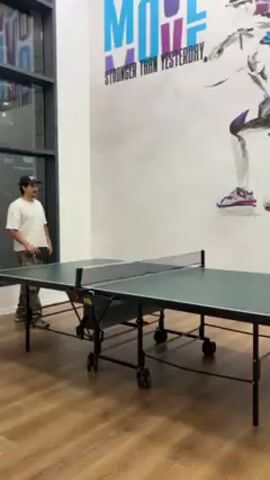 The video shows a recreational area with a ping pong table and a mural featuring athletes. The mural, in shades of gray with touches of blue and purple, depicts various figures engaged in athletic activities. A flat screen TV is mounted on the wall below the mural. The ping pong table is green with a black frame and net. The floor is wooden. A window is visible on the left side of the frame. A snippet of gameplay can be seen before the camera pans upwards to the mural.