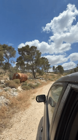 Vehicle travels dirt road past abandoned tank in Jordan