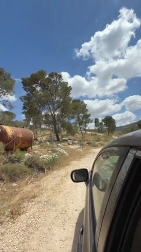Vehicle travels dirt road past abandoned tank in Jordan