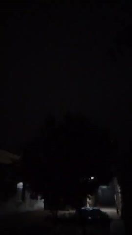 The video is extremely dark and blurry, making it difficult to discern many details. There are faint lights visible in the distance, suggesting an outdoor nighttime scene. Some blurry shapes in the lower part of the frame may indicate objects or people, but nothing is clearly identifiable. The overall impression is of a poorly lit and out-of-focus environment.