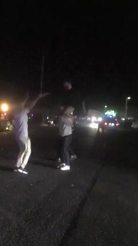 The video was taken at night and shows three men on a street. One man is holding what appears to be a long stick in the air, another man is carrying a third man on his shoulders. Cars and lights can be seen in the background. The men are moving around.