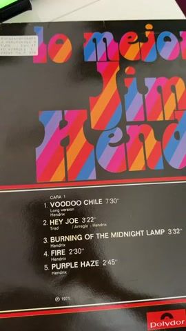 This is a close-up video of a record album cover. The album title "lo mejor de Jimi Hendrix" is displayed in large, colorful, striped letters. Below the title, the tracklist for "CARA 1" is visible. The tracks are "VOODOO CHILE" (Long version), "HEY JOE," "BURNING OF THE MIDNIGHT LAMP," "FIRE," and "PURPLE HAZE." The duration of each song is listed, along with the artist "Hendrix." The record company logo "Polydor" is in the bottom right corner. The video is shaky and blurry in parts.
