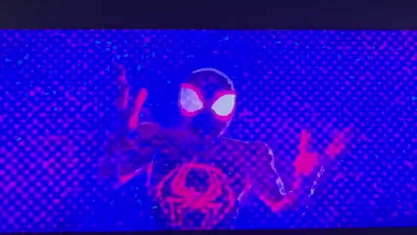 The video displays a dynamic, animated sequence with a strong emphasis on vibrant, contrasting colors, primarily deep blues and electric purples, with accents of bright pink and red.

The first scene features a figure in a black and red Spider-Man-like suit with glowing white eyes. The figure is in a dynamic pose, appearing to be in motion, possibly mid-action or in a dance-like movement. The background is a pixelated pattern of deep blue with scattered bright pink dots, creating a sense of digital or energetic space.

The second scene shifts to an interior setting. A person is seated in a chair, facing away from the camera, towards two computer monitors. This figure is entirely rendered in white, with a few black splotches on their arms and back, resembling a glitching or unfinished digital character. They are positioned in a room with a futuristic or laboratory-like feel, suggested by the geometric patterns and glowing lines in the background, which are a mix of purple and pink. The computer screens display complex, graphical interfaces with text and code, indicating a scene of data processing or digital interaction.

The third scene presents an abstract, symmetrical visual. Two metallic, red and blue objects, resembling nozzles or emitters, are positioned at the top and bottom of the frame, facing each other. Between them is a horizontally elongated, somewhat blurred blue shape. The background is a striking red field filled with a dense pattern of small white dots, creating a tunnel-like or portal effect.

The overall mood is energetic and futuristic, with a strong visual style that leans into digital art and animation aesthetics. The activity appears to be related to action, investigation, or digital manipulation, set within a stylized, non-realistic environment. There are no discernible cues about time of day or weather, and the emotions are conveyed through the intensity of the visuals and character poses rather than facial expressions. No legible text is visible in the video. The requested location context of Vozrozhdeniye, Russia, does not appear to be directly referenced or visually represented within the provided clips.