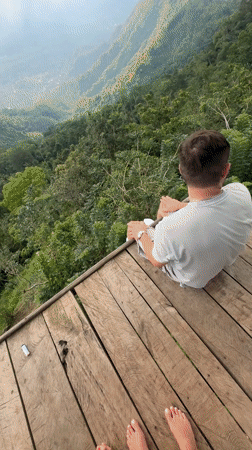 Three people relax on wooden platform overlooking Indonesian mountains