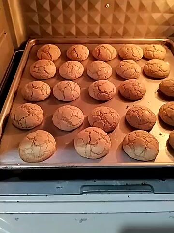 The video shows cookies being baked in an oven and then placed on a tray. A person is seen sitting on the floor, surrounded by baking ingredients, and appears to be making cookies. The scene suggests a home baking environment.
