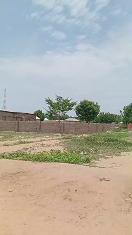 The video shows an outdoor scene with a building under construction in the background. The building is made of brick and has a wall surrounding it. There are trees and vegetation around the building. The sky is cloudy. The camera is panning from left to right.