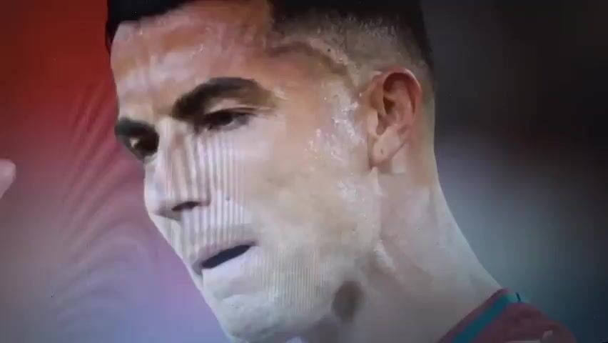The video shows a close-up of a digital rendering of a soccer player, likely from a video game. The player is sweating and appears to be reacting to an event on the field. He then turns and embraces another player, also digitally rendered. The scene is set within a stadium environment, with blurred spectators and stadium lights visible in the background. The overall impression is that of a moment of intense emotion or celebration within a virtual soccer match.