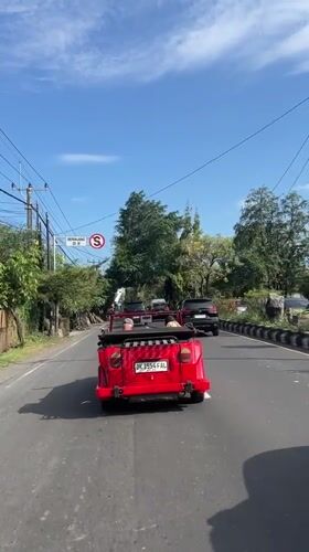 Red convertible drives through morning traffic in Denpasar, Indonesia