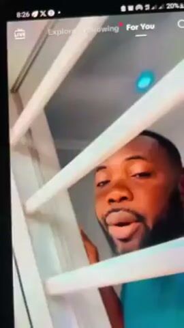 The video shows a dark-skinned man looking through white bars. The man has a beard and short hair. The video appears to be taken from a phone screen, as indicated by the user interface elements at the top of the screen, such as time, battery level, and social media navigation.