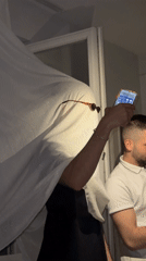 Person in white cloth holds smartphone indoors in Kalofer