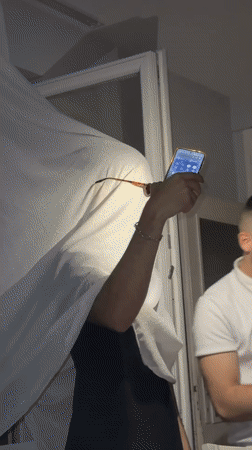 Person in white cloth holds smartphone indoors in Kalofer