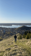 Visitors explore hillsides above Russian village on sunny afternoon