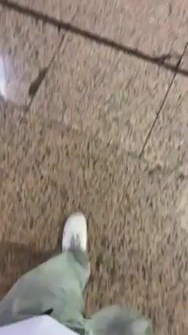 The video shows a first-person perspective of someone walking on a tile floor. The person is wearing white sneakers and light green pants. The tile floor appears to be inside a building.