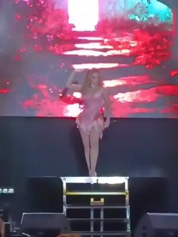 Here's a description of the video:

The video shows a woman on stage at what appears to be a concert or performance. She's wearing a short, pink outfit resembling a fairy costume, with what looks like leaves or petals as part of the design. She has long blonde hair and is standing on a platform made of flight cases.

Behind her is a large screen displaying changing visuals, which include what appears to be a fantastical forest scene with glowing elements. There's a person in a tank top walking towards the woman on stage. In front of the stage, you can see the heads and shoulders of a crowd. Stage lighting equipment is also visible.