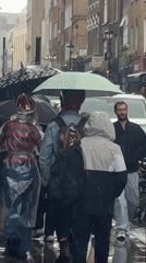 Londoners navigate rainy streets with umbrellas during afternoon shower
