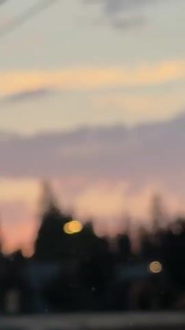 The video shows a view of the sky during sunset, with clouds colored pink and purple. In the foreground, there are trees and some buildings, and a "Do Not Enter" sign is visible. The camera is moving, creating a slightly blurry effect, and power lines are also present in the frame.