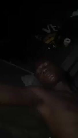 A dark, close-up shot shows a Black man lying down, possibly in bed. He is shirtless and his eyes are closed. Above him and slightly out of focus, there's a dark-colored item, possibly clothing, with the word "VE" visible in a yellow and black design. The general environment is dark and indistinct.