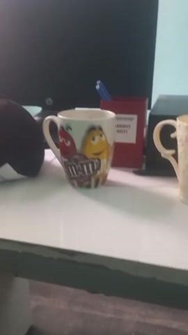 The camera pans from a desk with two mugs, a red pen holder, and a black plush object to a computer monitor. The monitor displays a dark screen with a candlestick chart on it. The chart shows a downward trend followed by a slight upward movement. The title of the chart appears to be “Market Gap BTC Dominance.” Below the monitor are two small black speakers.