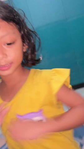 A young girl is joyfully dancing to music in a room. She is wearing a yellow t-shirt with an owl on it, and leopard-print shorts. Her hair is short and wet. She is smiling brightly and moves energetically to the beat of the music. A yellow toy duck is visible on the floor near a blue wall.