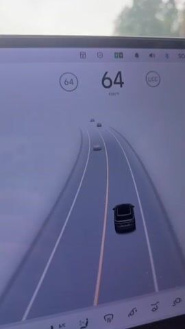 The video displays the interior and exterior view of a car driving on a highway. The interior view shows a car's dashboard with a speed indicator showing 64 km/h and a graphic representation of the car and surrounding vehicles on the road. The speed then changes to 63 km/h. The exterior view shows the car's perspective from the windshield, observing the road ahead with other cars, trees, and a cloudy sky. The car appears to be in motion, navigating through traffic.
