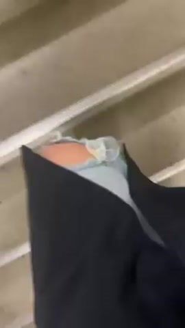 The video depicts a person descending a set of indoor stairs. The stairs are gray with silver or aluminum strips along the edge of each step. The person is wearing dark pants and a light-colored shirt. Brown shoes are visible. The camera is pointed downwards, capturing the steps and the lower part of the person's body as they move.
