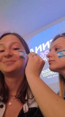 Women apply Israeli flag face paint near Eurovision Vienna signage