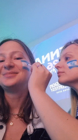 Women apply Israeli flag face paint near Eurovision Vienna signage