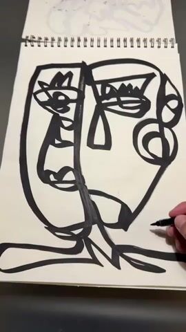 A hand holds a black marker and draws a signature on a piece of paper in a spiral notebook. The paper contains a large black and white abstract drawing of a face. The notebook is open and lying on a dark surface.